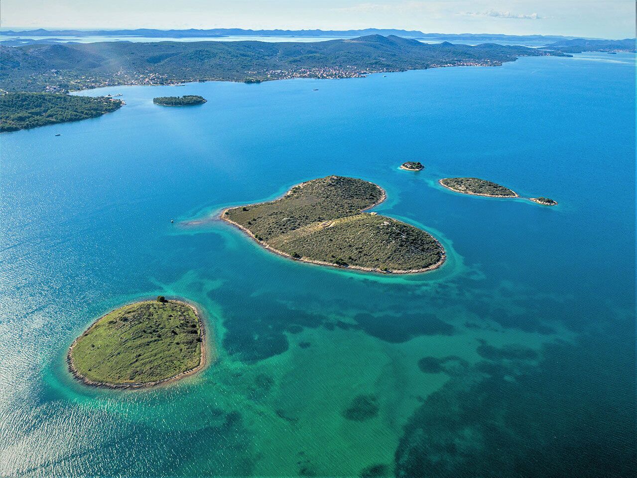 Luftaufnahme einer Küstenregion mit mehreren kleinen Inseln, umgeben von klarem, blauem Wasser.