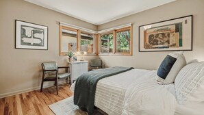 Un dormitorio con cama, escritorio, silla y dos ventanas.