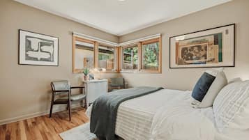 A bedroom with a bed, a desk, a chair, and two windows.