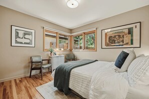 Une chambre à coucher avec un lit, un bureau, une chaise et deux fenêtres.