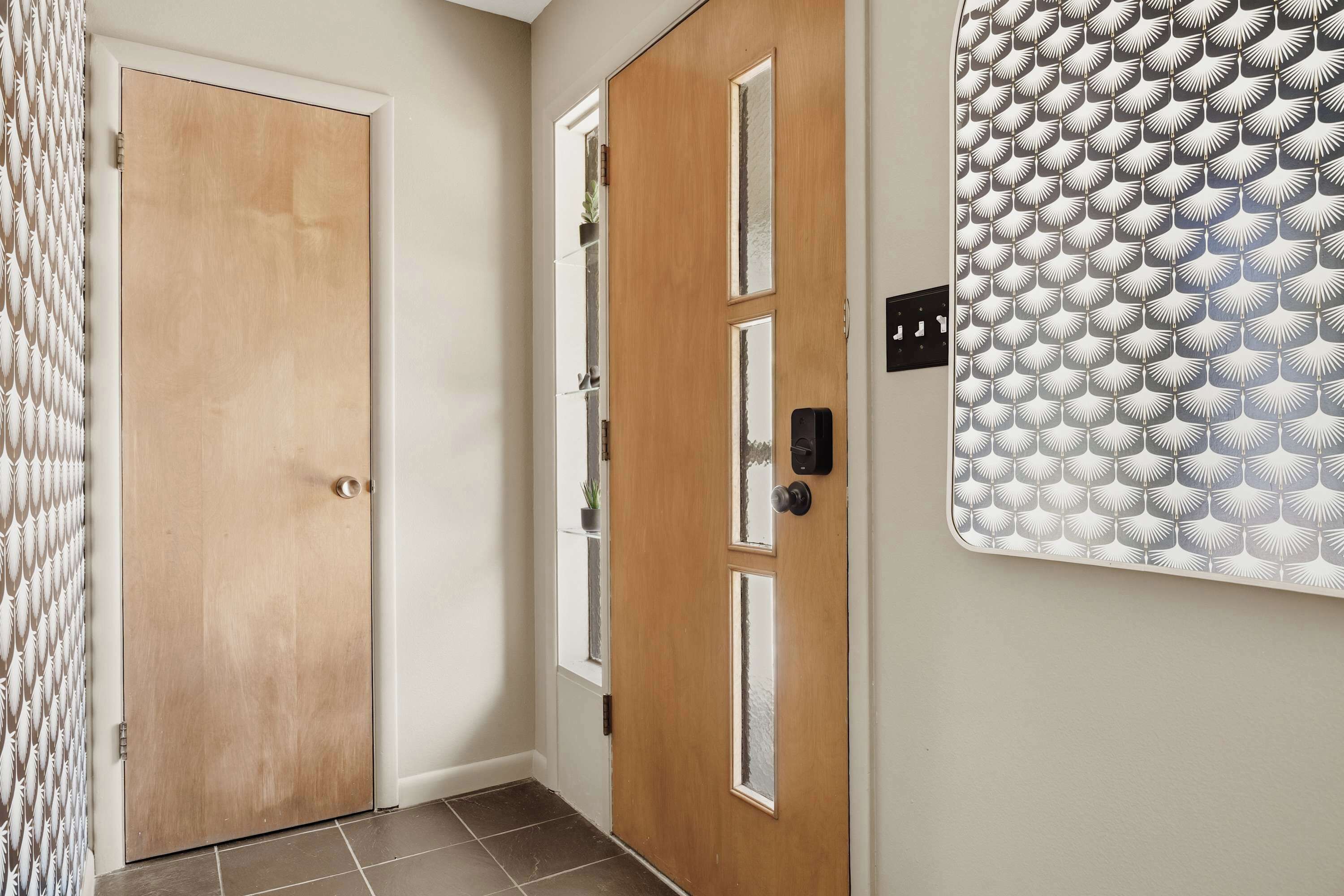 A hallway with a wooden door, a glass door with a window, and a patterned wall.