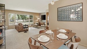 Un comedor con una mesa dispuesta para cuatro personas, un sofá y un televisor al fondo.
