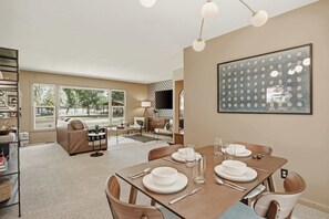 Un coin repas avec une table dressée pour quatre personnes, un canapé et un téléviseur en arrière-plan.