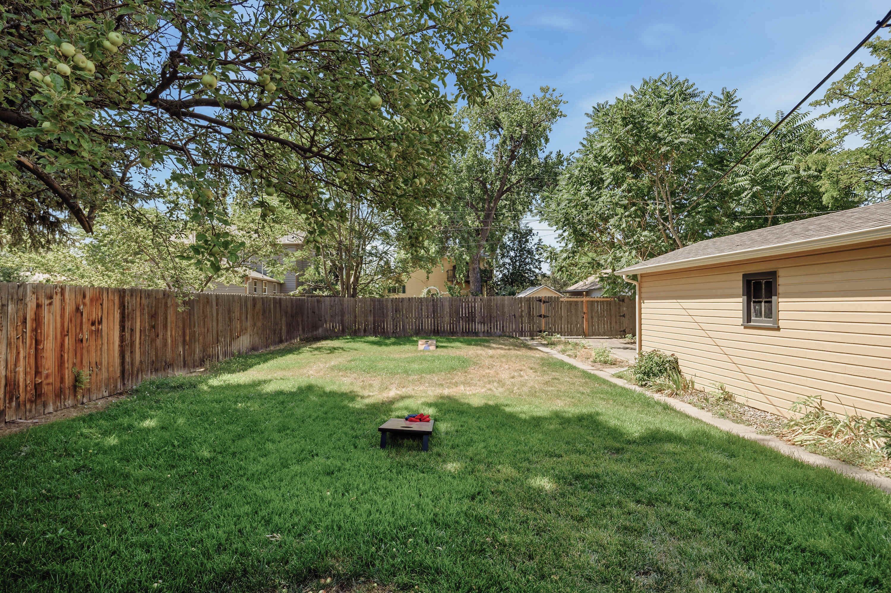 A backyard with a wooden fence, a grassy lawn, and a small table with red objects.