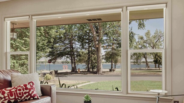 Una habitación con un sofá de cuero, una mesa de centro de vidrio con libros y vistas a un parque y un lago a través de amplias ventanas.