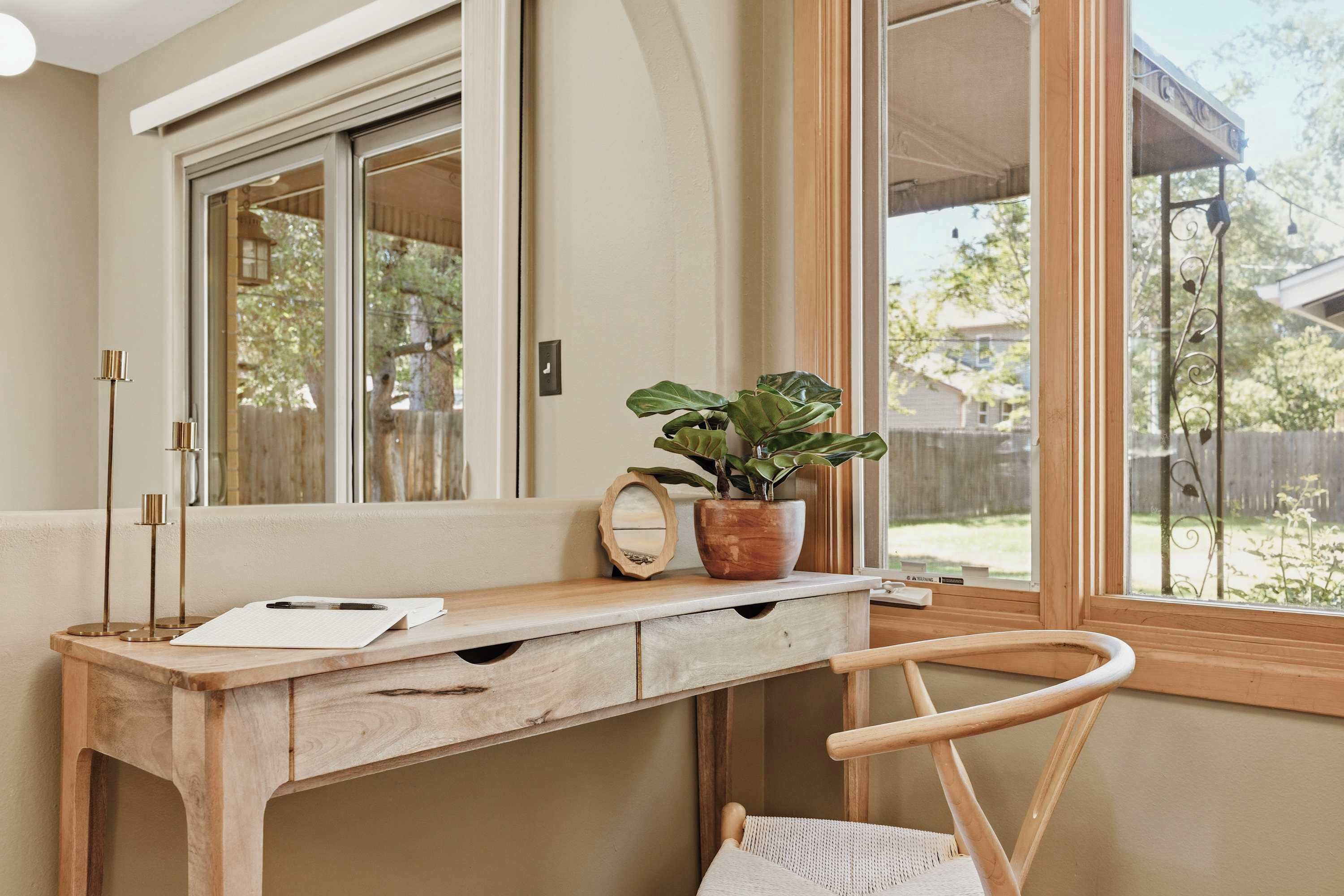 Een houten bureau met een spiegel, een plant in pot en een stoel in een kamer met een raam.