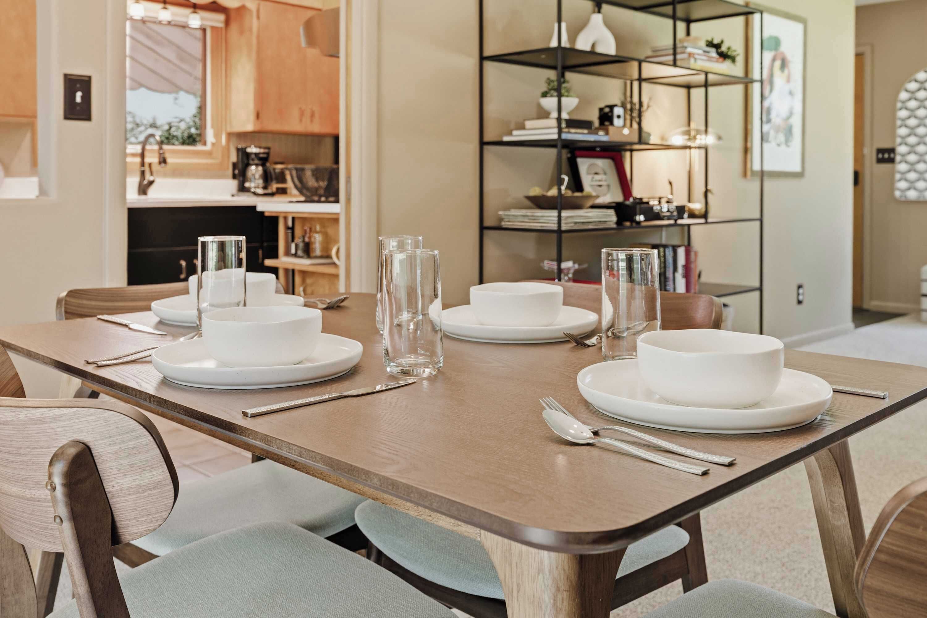 A dining table set with white plates, bowls, and glasses, with chairs around it.