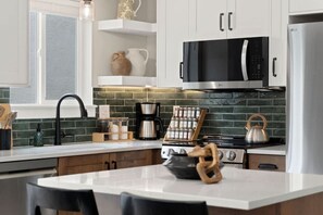 A modern kitchen with white cabinets, a black microwave, a stainless steel kettle, and a coffee maker. - Renovated Executive Rental Near CSU (Fort Collins)