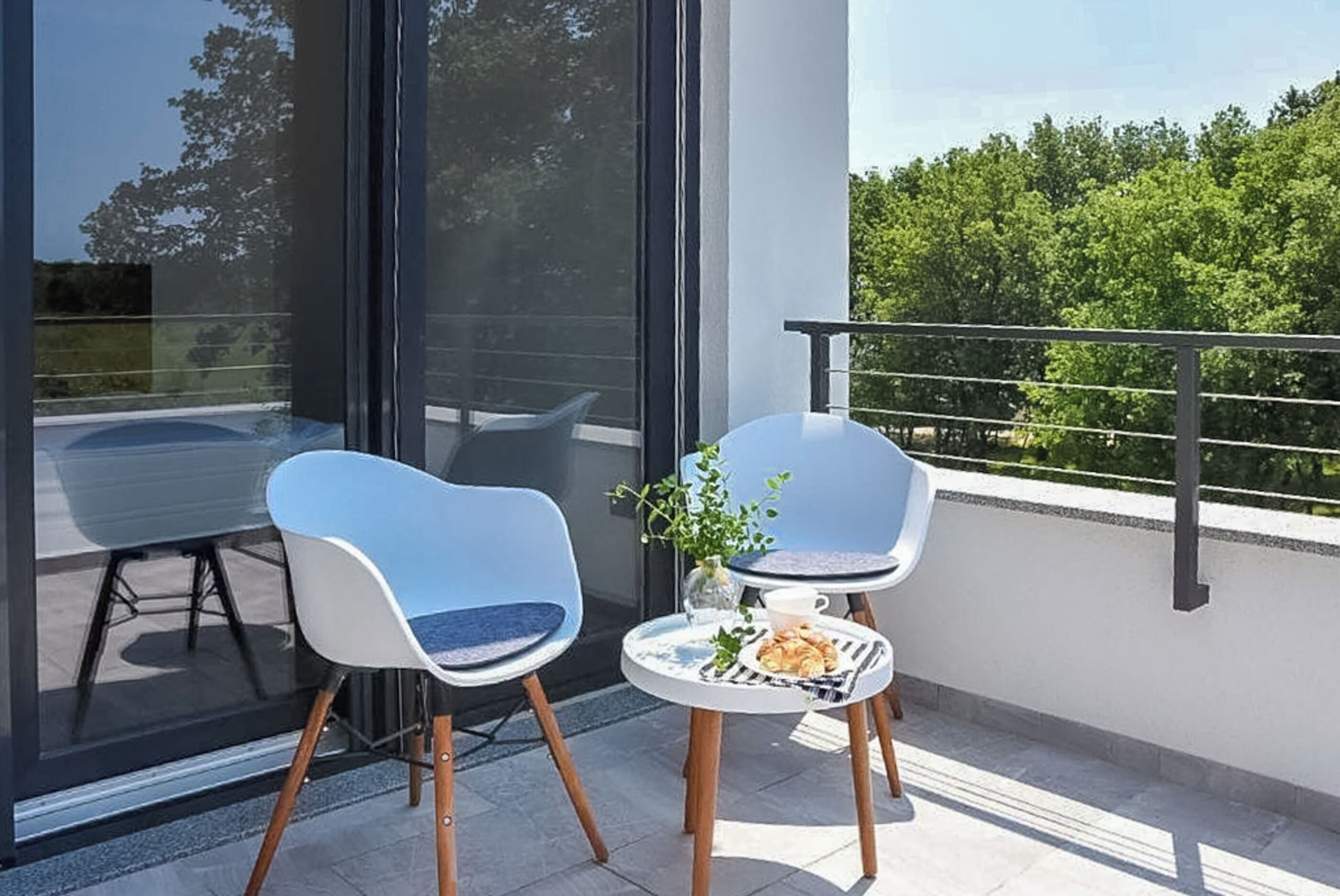 A balcony with two chairs, a small table with a plant and a cup, and a glass door leading to an outdoor area.