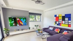 Una sala de estar moderna con un televisor de pantalla plana grande, un sofá, una mesa de centro y un cuadro abstracto y colorido en la pared.