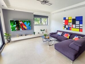 A modern living room with a large flat-screen TV, a sofa, a coffee table, and a colorful abstract painting on the wall. - Villa Tara (Medulin)