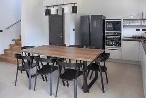 A modern kitchen with a wooden dining table and black chairs, a built-in oven, and a staircase leading to another level. - Villa Tara (Medulin)