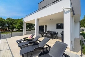A covered outdoor area with lounge chairs, a table, and a grill. - Villa Tara (Medulin)