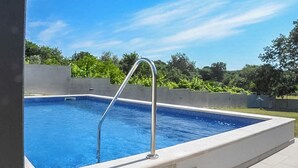 Una piscina rectangular con una escalera metálica, rodeada por un muro bajo y un suelo de baldosas.