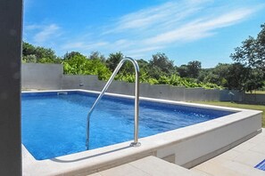 A rectangular swimming pool with a metal ladder, surrounded by a low wall and a tiled deck. - Villa Tara (Medulin)