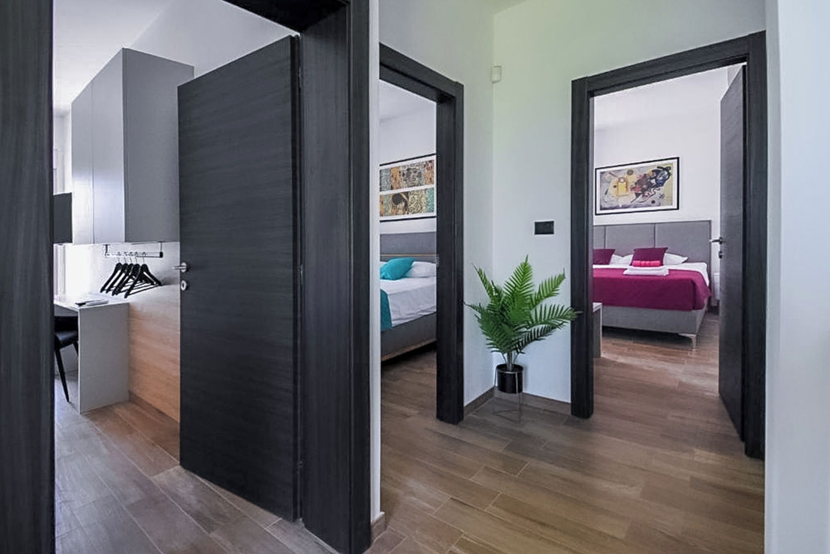 A modern hotel room with a wooden floor, a desk with a chair, a bed with a headboard, and a potted plant.