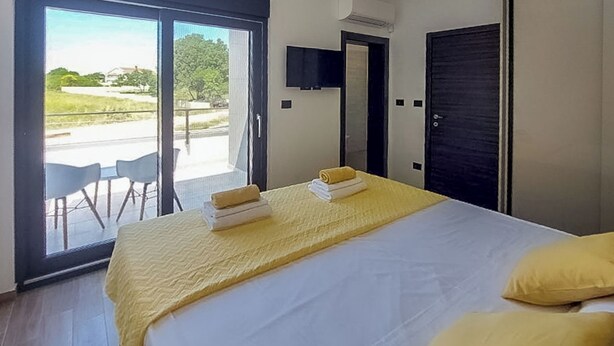 Una habitación de hotel con cama, ventana con vistas, puerta y una silla afuera.