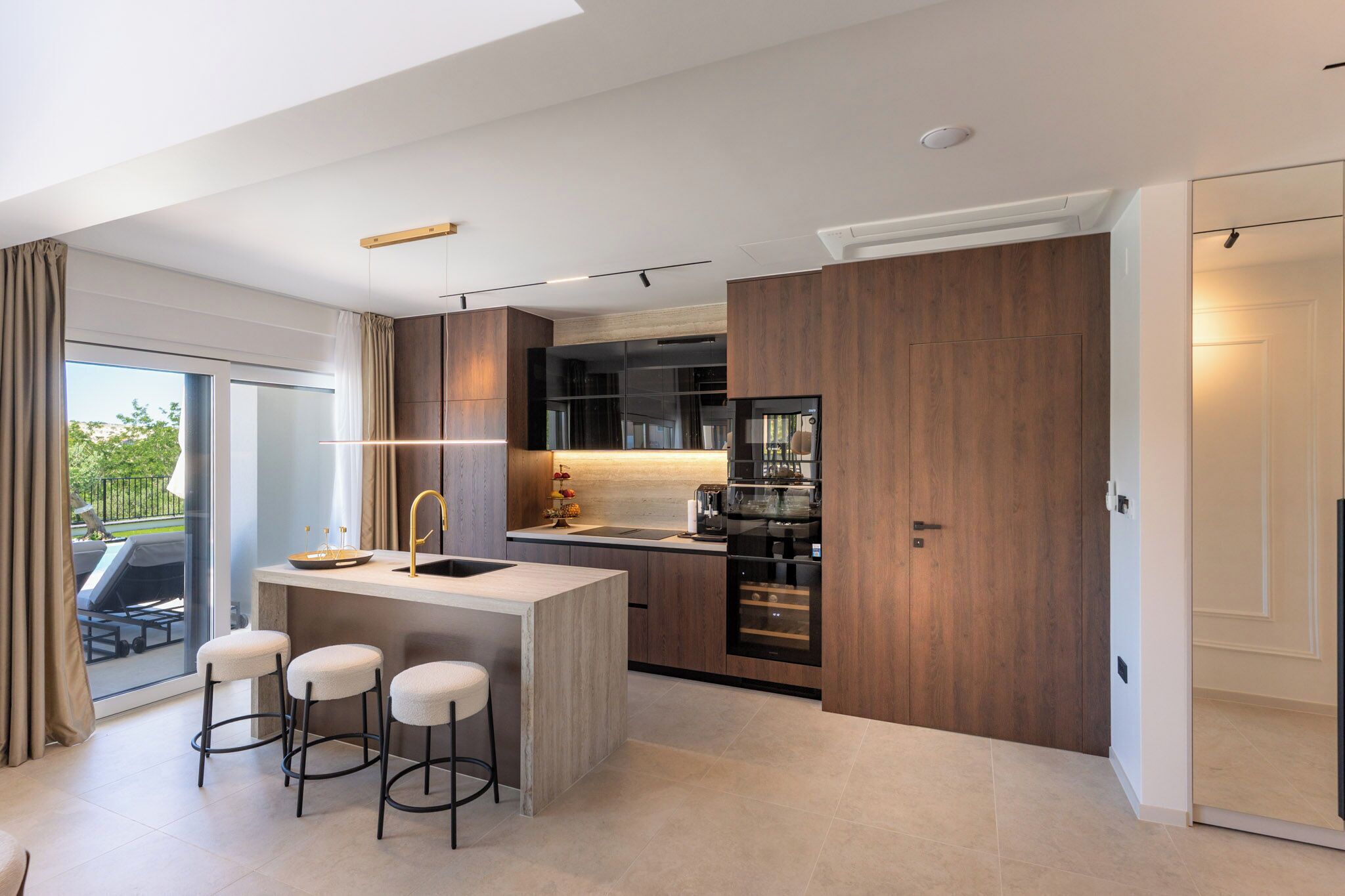 Una cocina moderna con una isla central, taburetes de bar y un ventanal corredero que da a un espacio exterior.