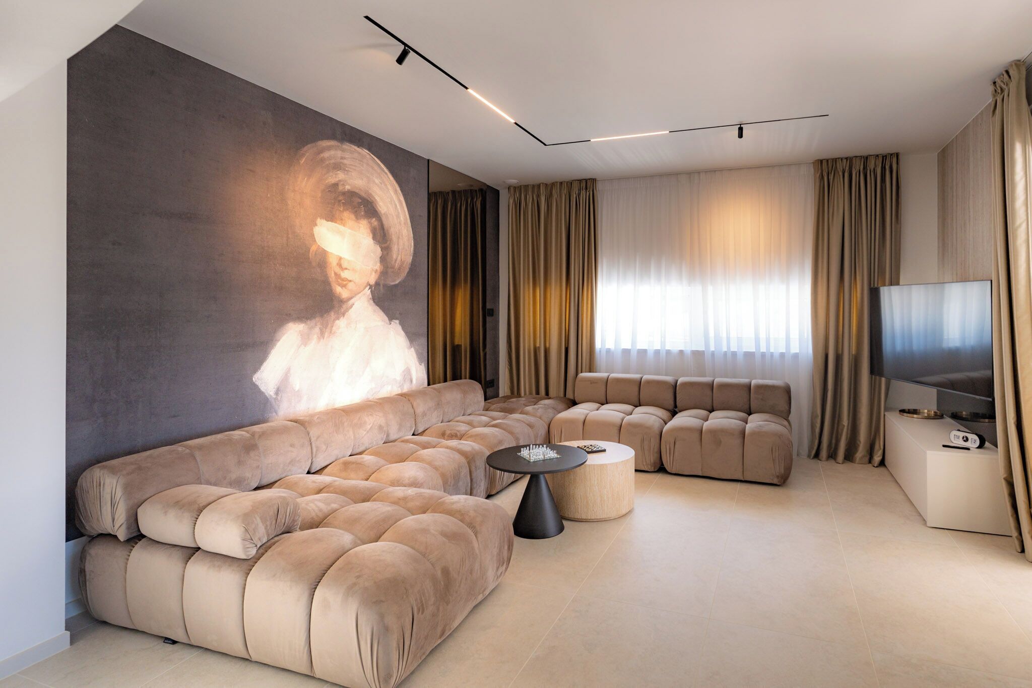 A modern living room with a large sectional sofa, a flat-screen TV, and a wall-mounted projector.