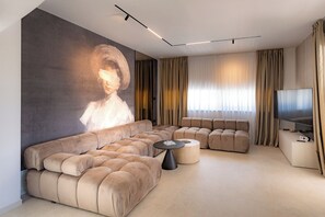 A modern living room with a large sectional sofa, a flat-screen TV, and a wall-mounted projector.