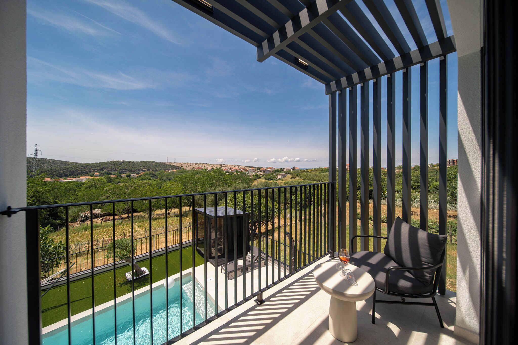 A balcony with a pool, outdoor furniture, and a view of a green landscape.