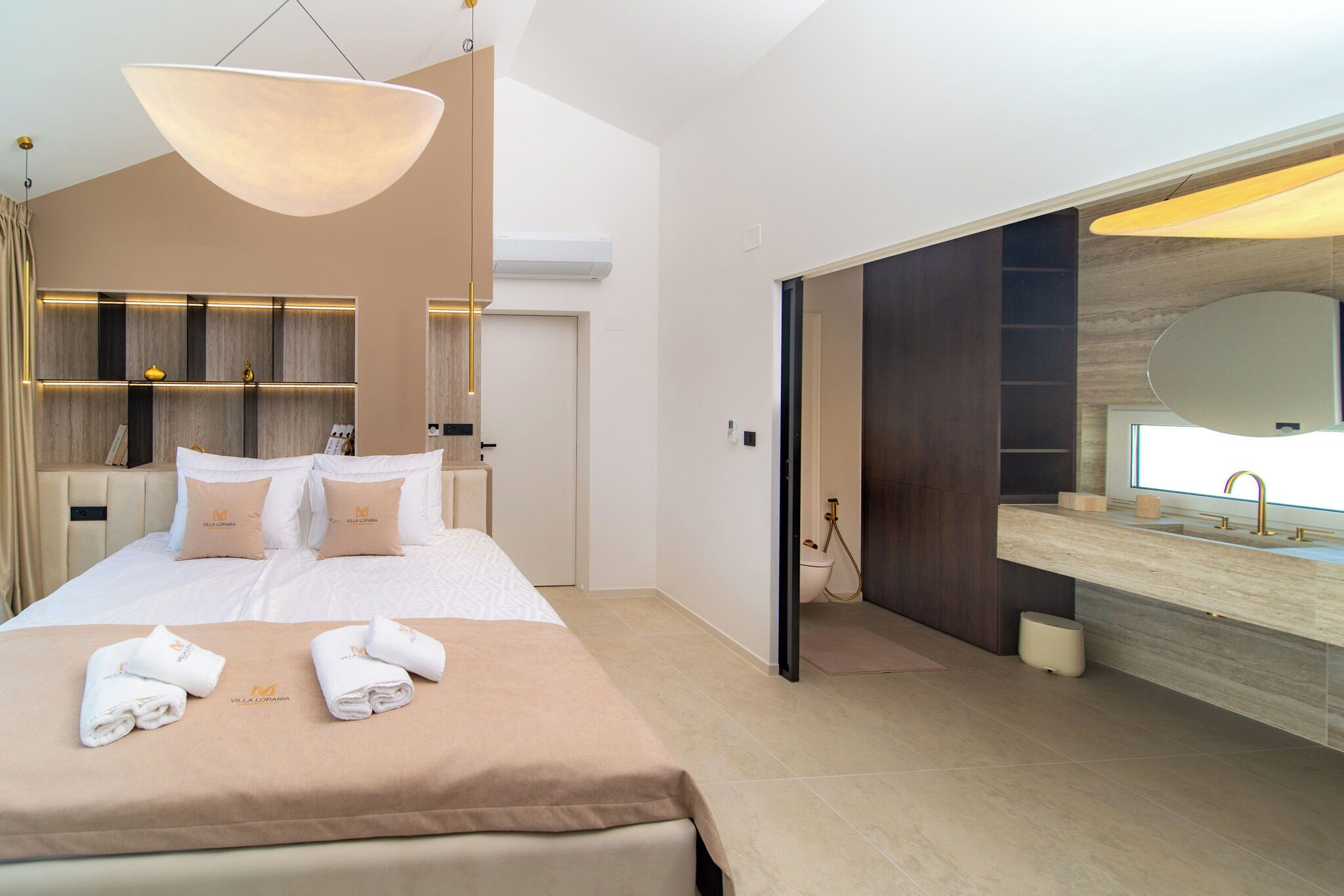 A hotel room with a bed, bedside tables, a large mirror, and a bathroom with a sink and shower.