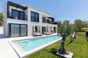Una casa moderna de dos pisos con piscina, mobiliario exterior y césped cuidado.
