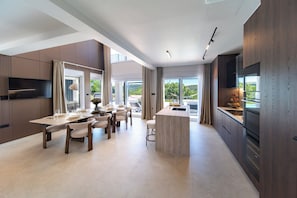 A modern kitchen with a dining area, large windows, and a flat-screen TV.