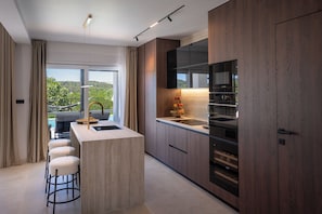 Una cocina moderna con una isla central, taburetes de bar, un ventanal y vistas a la vegetación.
