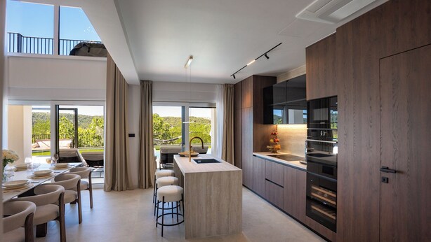 A modern kitchen with a central island, bar stools, and a dining area with a view of greenery. - Villa Loparia (Lopar)