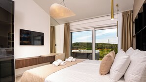 A modern hotel room with a large bed, a desk, and a view of a green landscape through large windows. - Villa Loparia (Lopar)