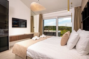 A modern hotel room with a large bed, a desk, and a view of a green landscape through large windows. - Villa Loparia (Lopar)