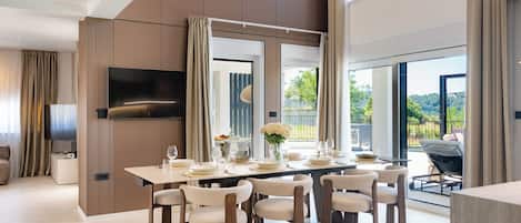 A modern dining room with a large table set for six, a flat-screen TV, and a view of the outdoors.
