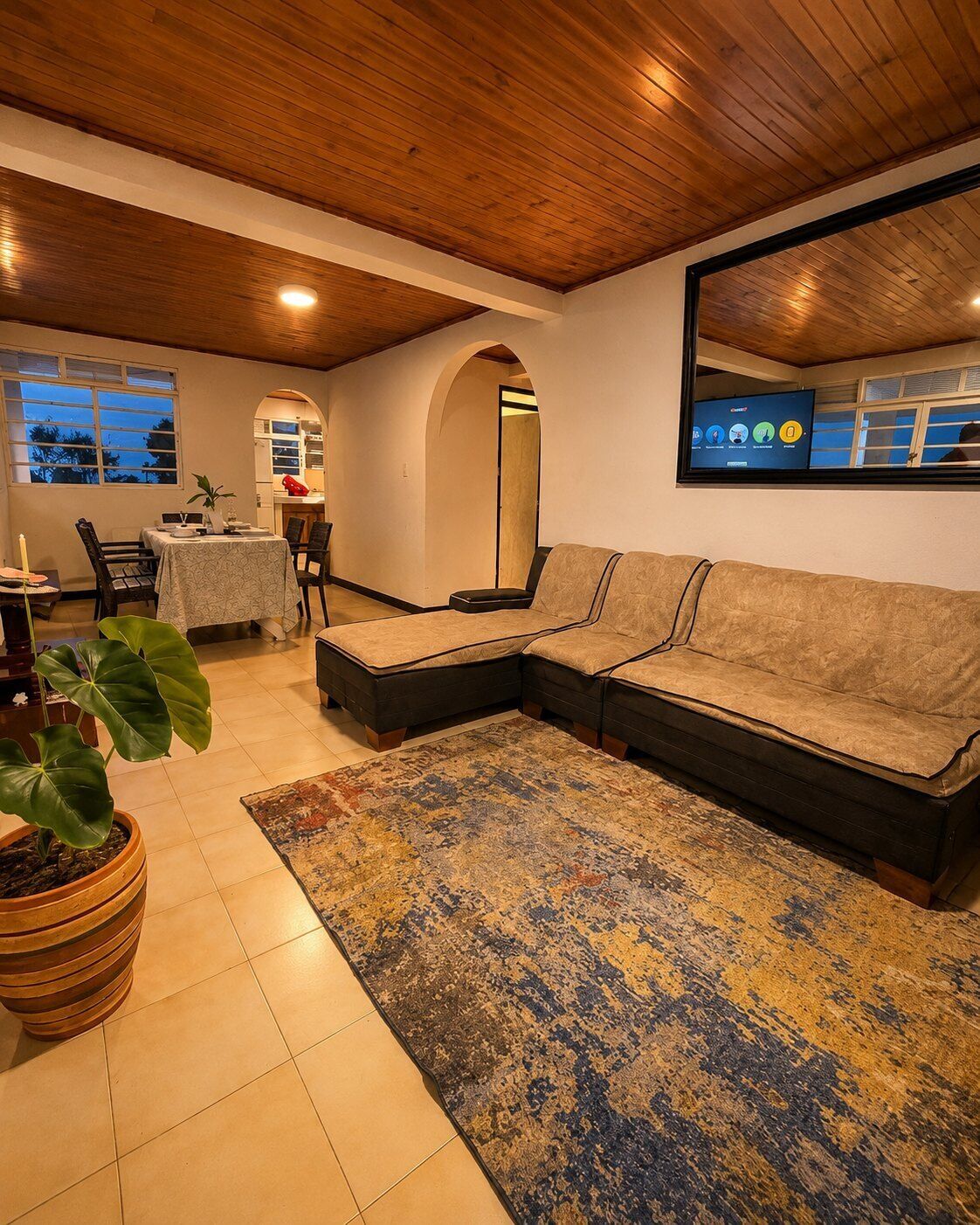 A living room with a sectional sofa, a dining table, and a large mirror.