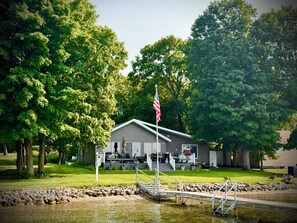 A lakeside lodge with a dock, surrounded by trees and a flag. - Cozy lake cabin with 50 Amp for RVs on Pelican Lake, with private dock. (Detroit Lakes)