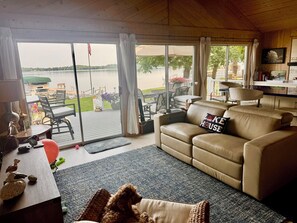 A cozy living room with a leather sofa, a dining area with outdoor seating, and a view of a lake. - Cozy lake cabin with 50 Amp for RVs on Pelican Lake, with private dock. (Detroit Lakes)