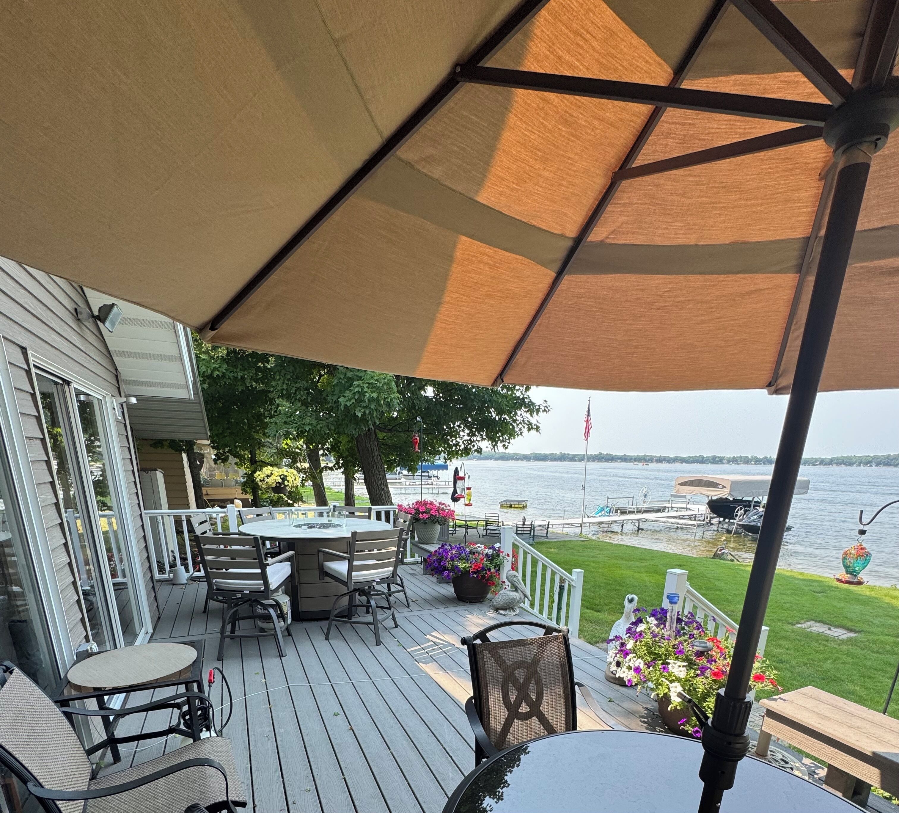 A covered outdoor deck with a table and chairs, overlooking a body of water.