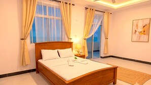A bedroom with a wooden bed, two windows with curtains, a bedside table with a lamp, and a painting on the wall. - Private 2-bedroom Beachfront Apartment in Uroa, Zanzibar (Uroa)