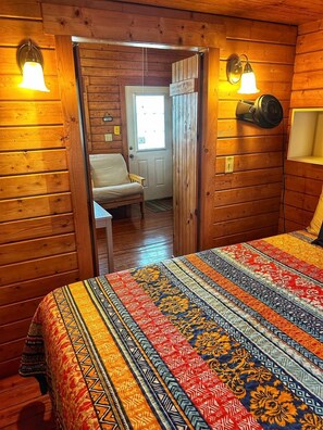 Une pièce en bois contenant un lit, une chaise et une porte donnant sur une autre pièce.