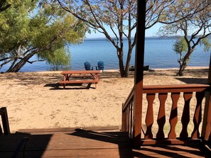 A beach view with a wooden deck, a picnic table, and two chairs.