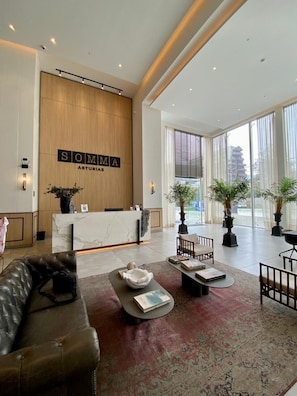 En moderne hotellobby med reception, læderpolstrede møbler, store vinduer og potteplanter.