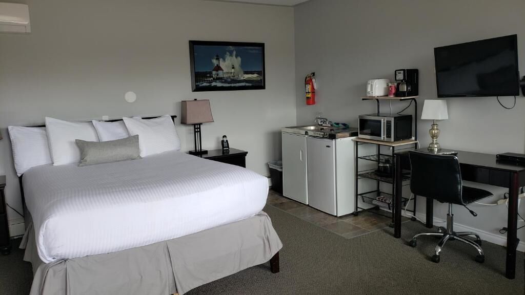 A hotel room with a bed, a desk, a television, a microwave, and a fire extinguisher.