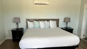 A bedroom with a large bed, two bedside tables with lamps, a wall-mounted air conditioner, and a door to the right. - Middleton Motel and Suits (Middleton)
