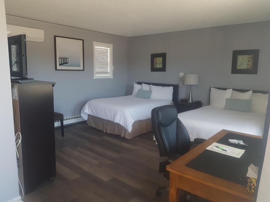 A hotel room with two beds, a desk, a chair, a TV, and a refrigerator.