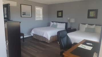 A hotel room with two beds, a desk, a chair, a TV, and a refrigerator.
