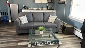 A living room with a sofa, a glass coffee table, a kitchen area with a microwave, and a window. - Middleton Motel and Suits (Middleton)