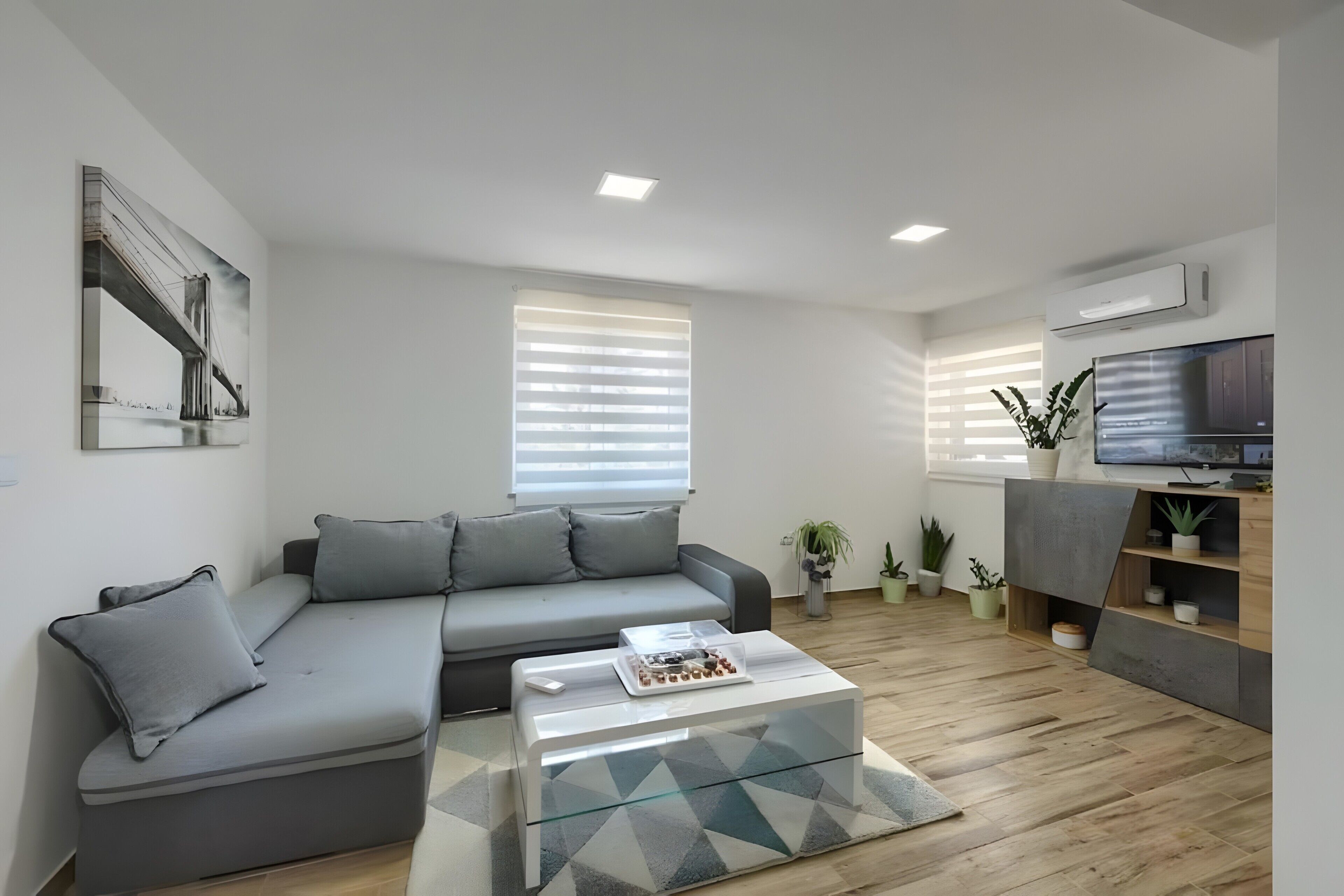 Ein modernes Wohnzimmer mit einem grauen Ecksofa, einem Glastisch und einem Flachbildfernseher.