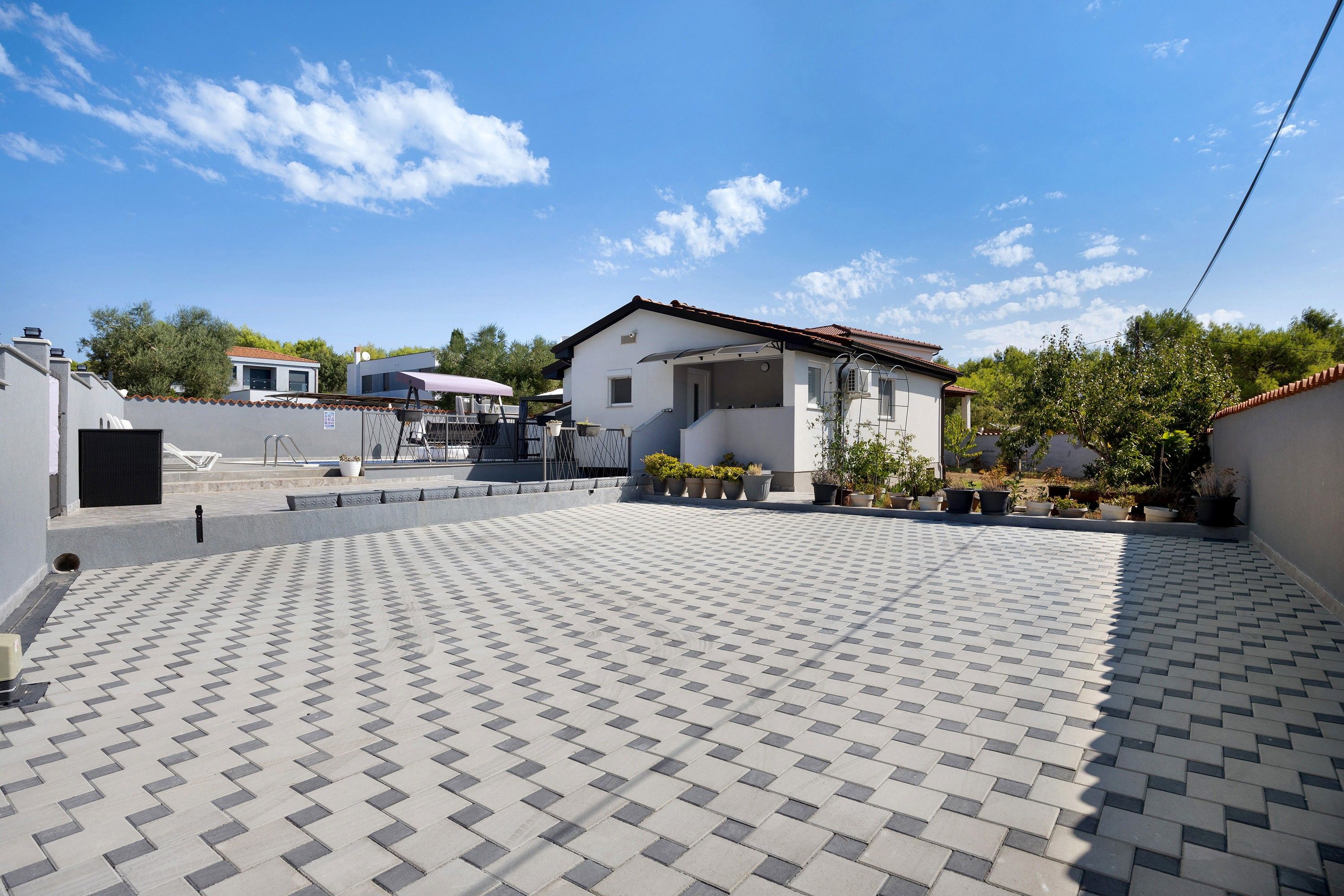 A residential area with a paved courtyard, a house with a tiled roof, and potted plants.