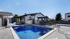 Piscina com boia de cisne, área de estar coberta e prédio com telhado telhado.