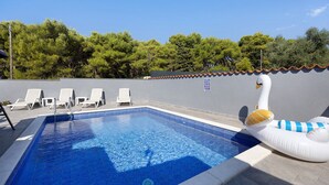 Piscina com água azul cristalina, rodeada por cadeiras de lounge brancas e um boi-mórbido decorativo.
